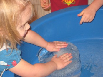Ett barn utforskar en stor isklump i en balja med vatten inne på förskolan